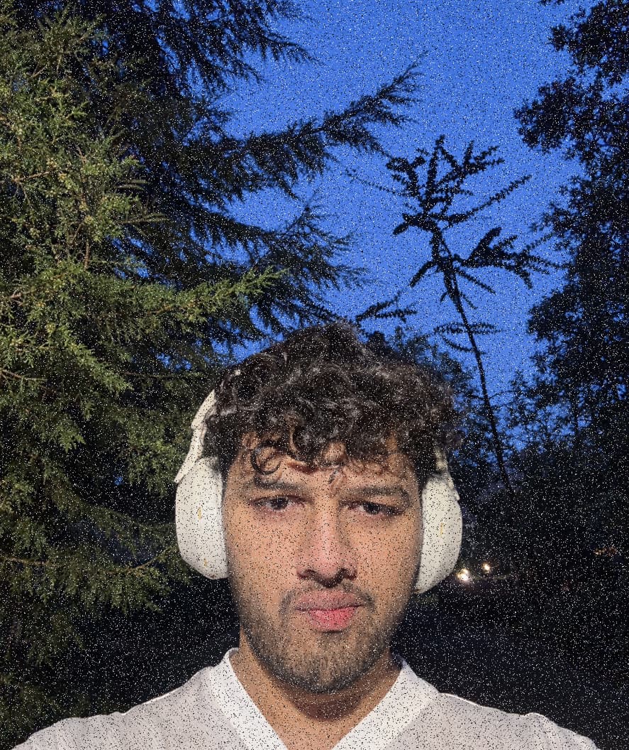 Sahil outdoors at dusk in white over-ear headphones, pines and a deep blue sky behind him